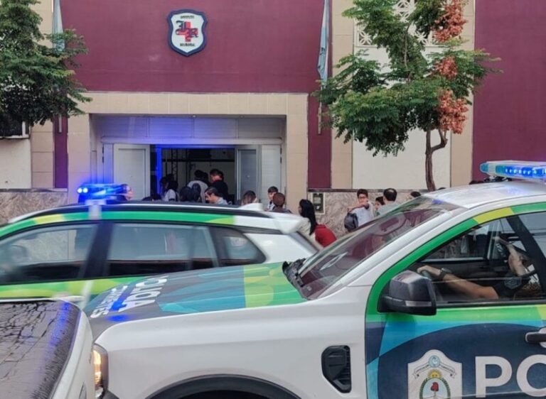 Estudiantes ingresando a una escuela en Corrientes bajo la lluvia, con presencia policial en el acceso.
