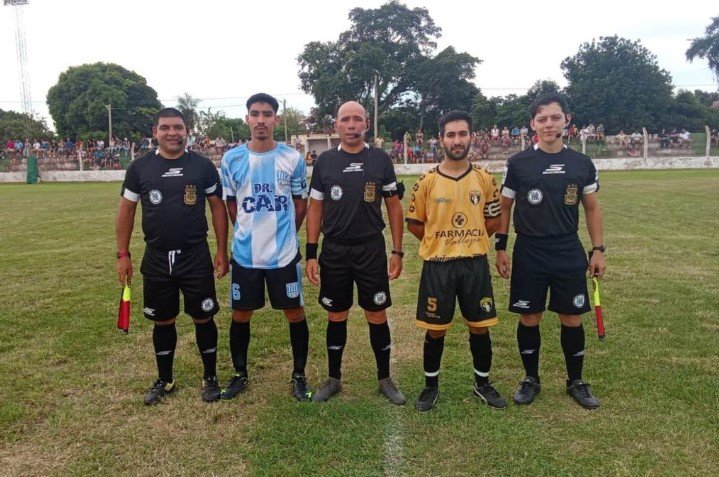 Árbitros de fútbol ingresando a un campo de juego en un partido de liga regional